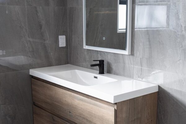 Contemporary bathroom vanity installation with woodgrain drawers and LED mirror by Stanton Builders
