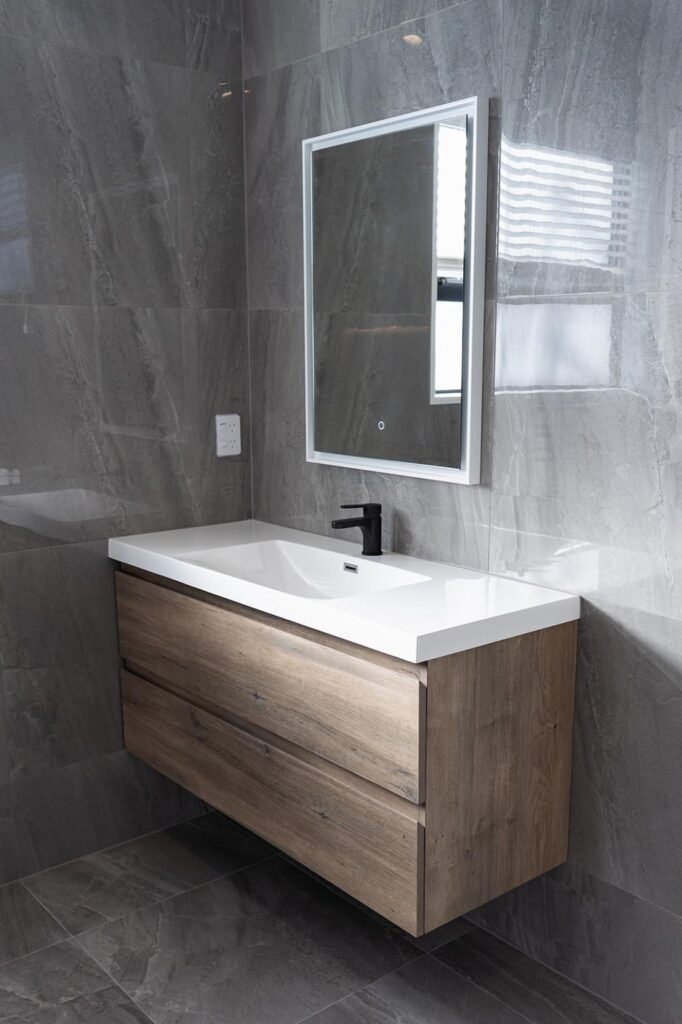 Contemporary bathroom vanity installation with woodgrain drawers and LED mirror by Stanton Builders